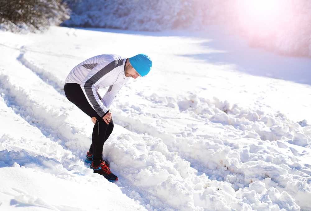 Man clutching his knee in discomfort while standing in a snowy landscape, illustrating how cold weather can worsen arthritis pain.