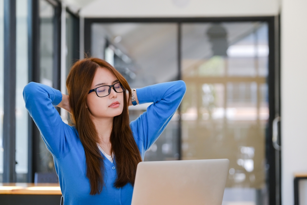Office worker stretching neck and shoulders at desk to relieve back pain—part of orthopedic exercises for desk job health.