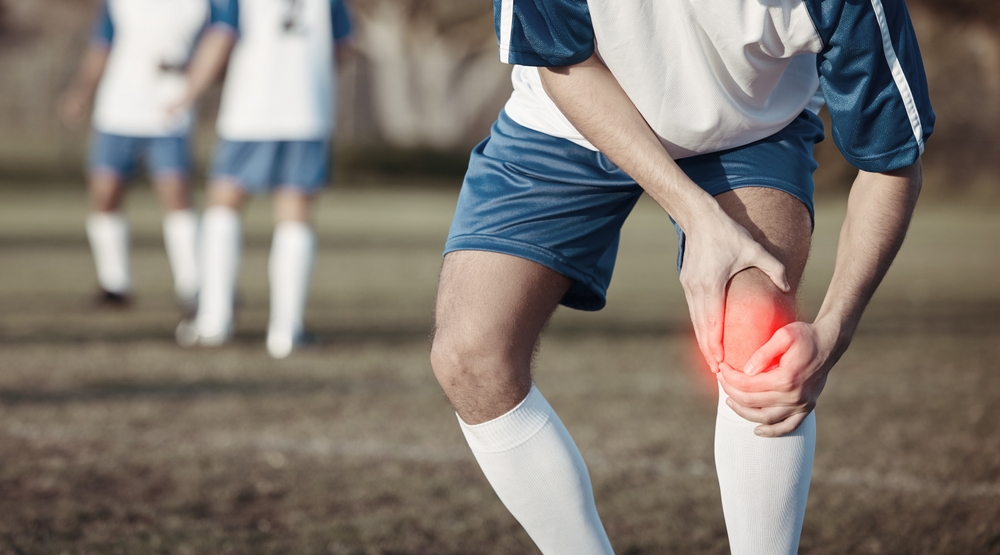 Soccer player clutching knee in pain after a suspected knee ligament injury during a game