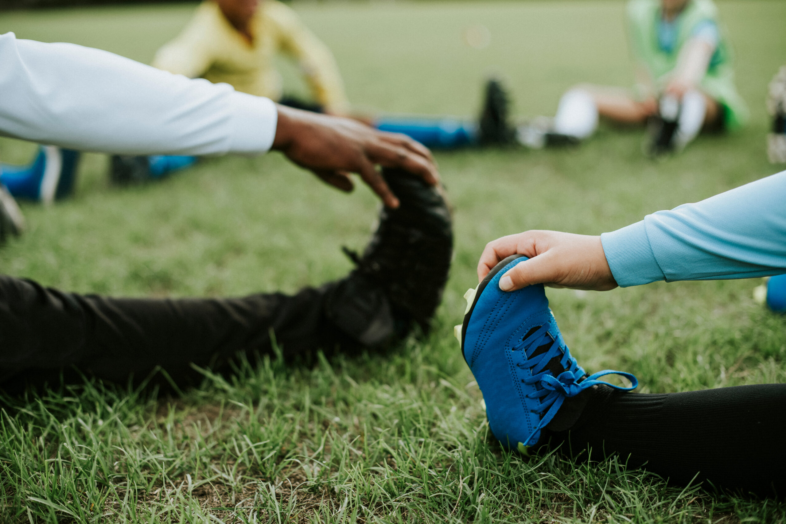Young athletes stretching on a grassy field during spring sports practice to help prevent injuries.