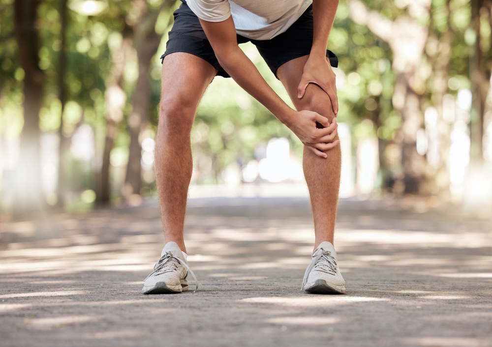 Person experiencing knee pain while walking outdoors